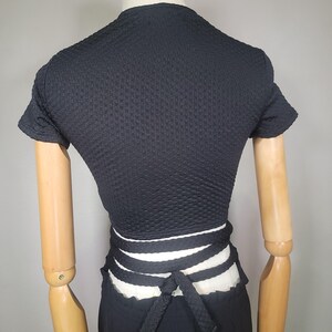 May include: Black short-sleeved crop top with a white and black wrap tie at the waist.