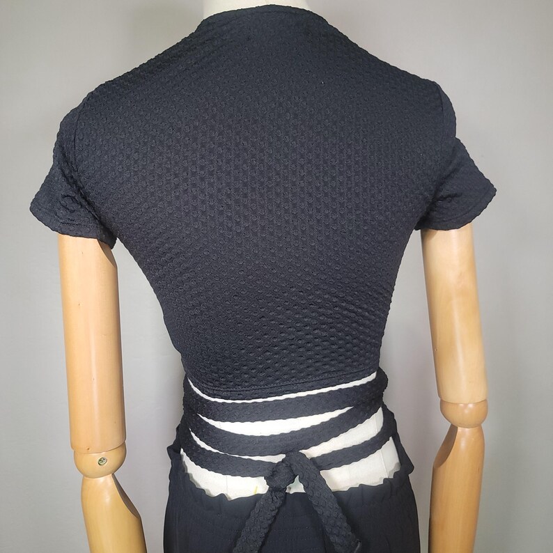 May include: Black short-sleeved crop top with a white and black wrap tie at the waist.