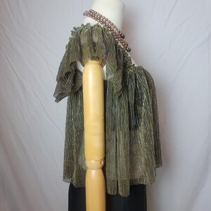 May include: A gold and black pleated top with ruffled sleeves is displayed on a mannequin. The top has a metallic sheen and a square neckline. A multi-strand beaded necklace in shades of brown and black is also visible.