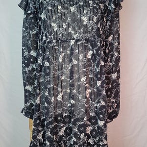 Puede incluir: Vestido con estampado floral en blanco y negro con mangas largas y cuello con volantes. El vestido se exhibe en un maniqu&iacute;. El vestido tiene un volante escalonado en el dobladillo y un delicado collar plateado.