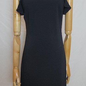 May include: A solid black sleeveless dress featuring a high neckline, thin shoulder straps, and ruffled cap sleeves. The garment has a fitted bodice that transitions into a flared, ruffled hemline at the bottom, providing a structured silhouette.