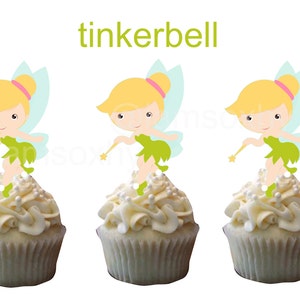 May include: Three cupcakes decorated with white frosting and pearl sprinkles. Each cupcake has a Tinkerbell character topper with blonde hair, a green dress, and fairy wings.