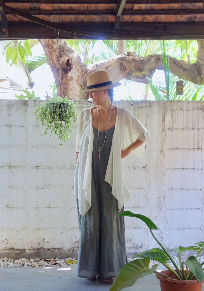 Puede incluir: Una mujer con un kimono de lino blanco sobre un mono gris. Lleva un sombrero de paja de ala ancha y un collar de plata.
