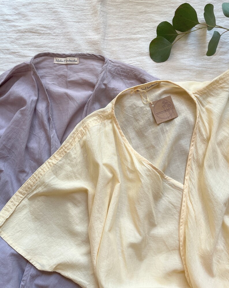 Puede incluir: Dos blusas de algod&oacute;n, una de color morado claro y otra de color amarillo p&aacute;lido. Ambas blusas tienen cuello en V y mangas cortas. Las blusas tienen una etiqueta que dice "Maka Handmade".