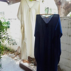 Puede incluir: Dos vestidos largos de lino holgados colgados de un tendedero. El vestido de la izquierda es blanco y el de la derecha es azul oscuro.