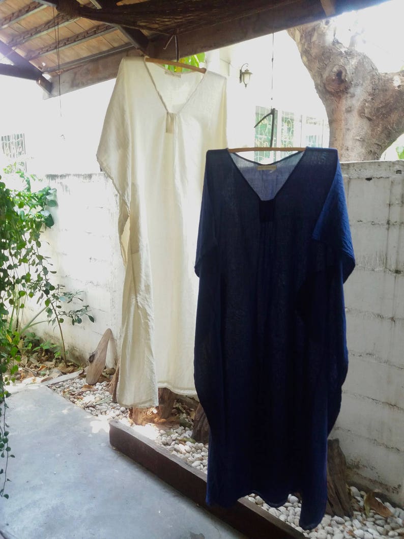 Puede incluir: Dos vestidos largos de lino holgados colgados de un tendedero. El vestido de la izquierda es blanco y el de la derecha es azul oscuro.