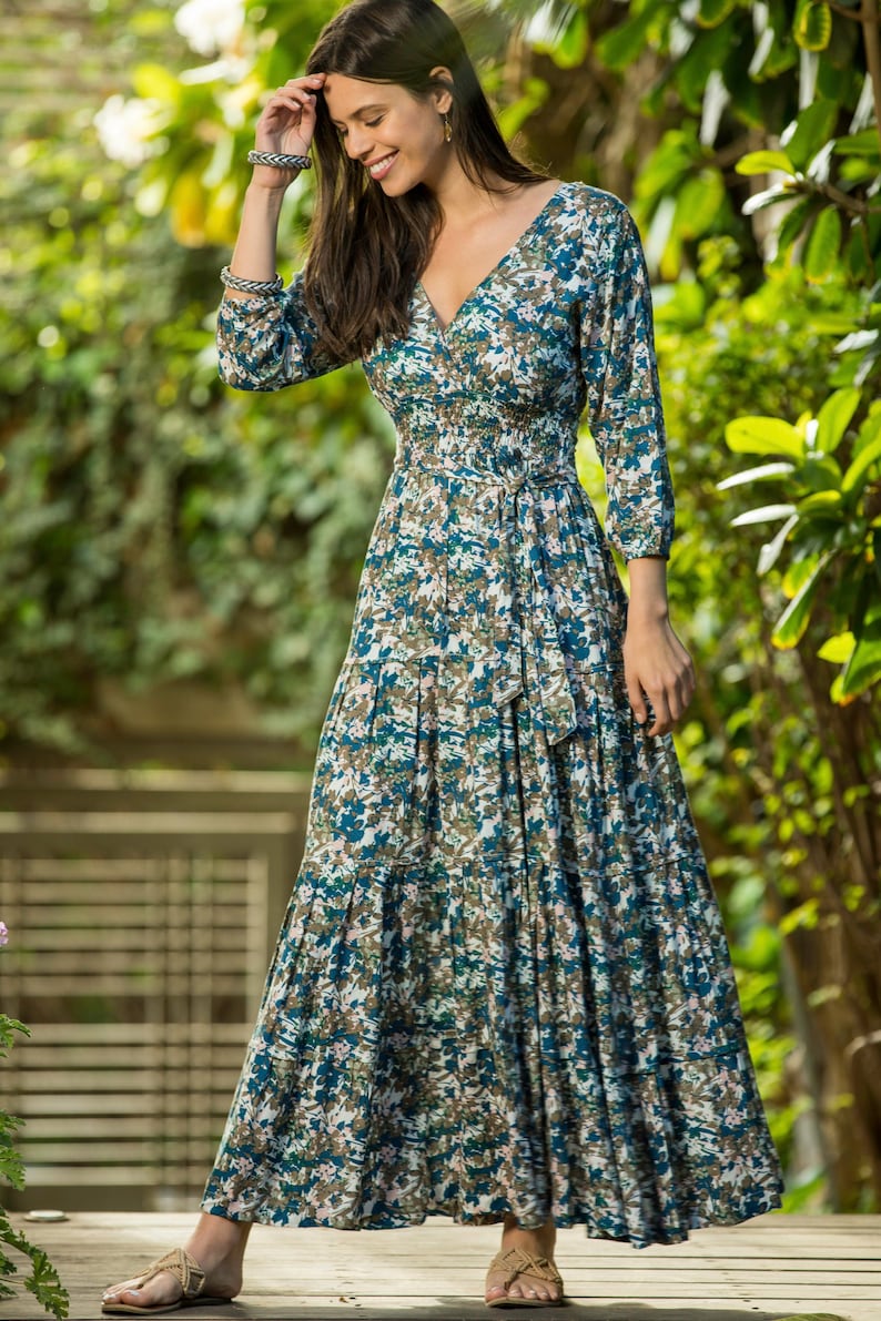 May include: A long, flowing maxi dress with a floral print in shades of blue, green, and white. The dress has a V-neckline, 3/4 sleeves, and a tie belt at the waist.