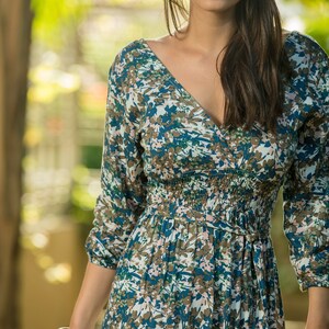 May include: A woman wearing a long-sleeved, blue and white floral dress with a V-neckline. The dress has a cinched waist and a tiered skirt.