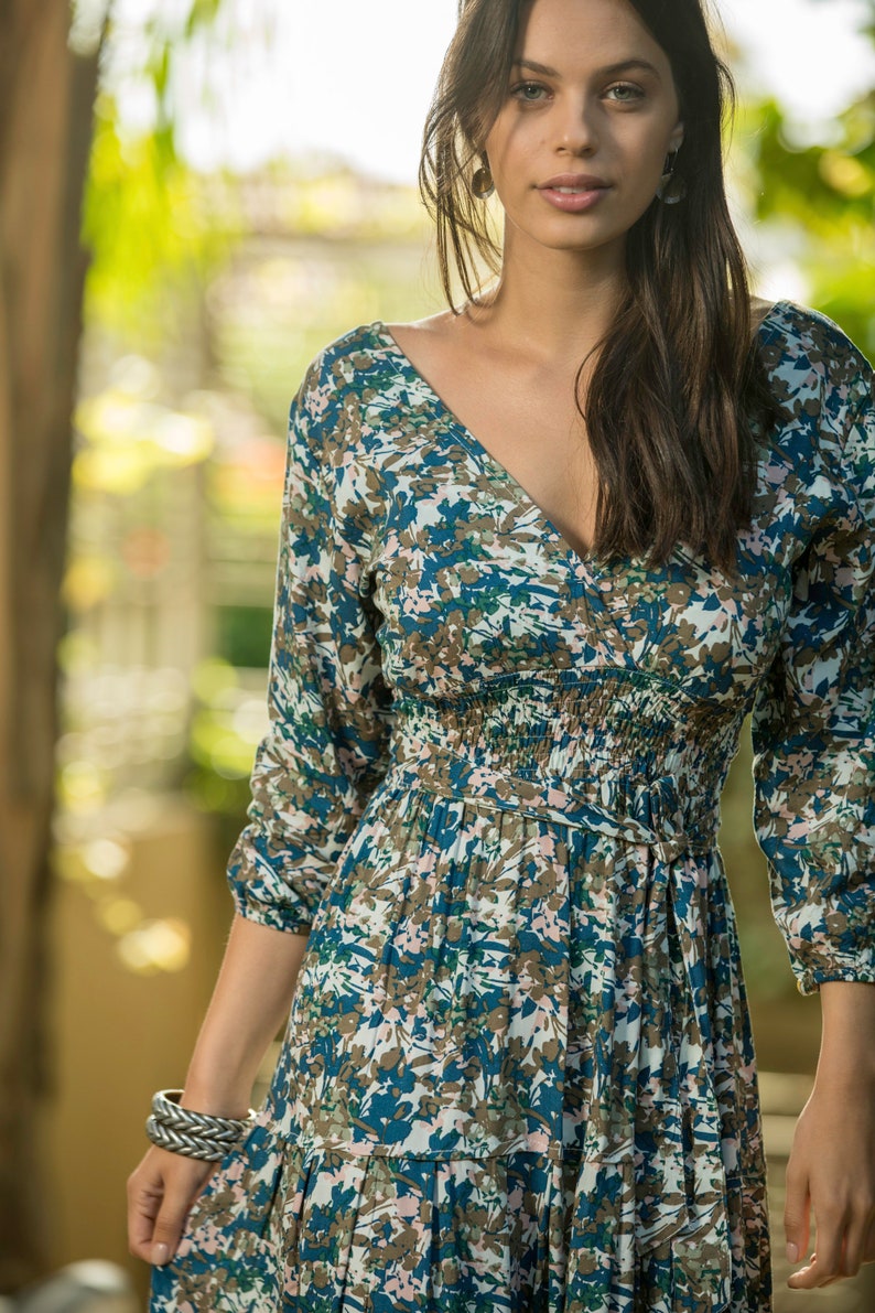 May include: A woman wearing a long-sleeved, blue and white floral dress with a V-neckline. The dress has a cinched waist and a tiered skirt.