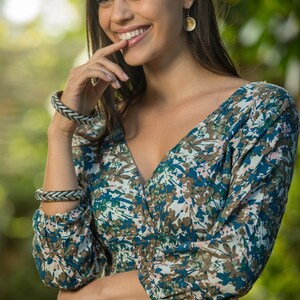 May include: A woman wearing a blue and brown floral print dress with a v-neckline and long sleeves. She is wearing two silver bracelets on her left wrist and a pair of gold earrings.