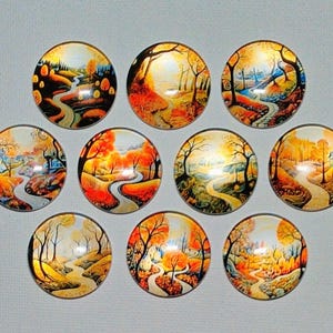 May include: A collection of ten round glass cabochons, each featuring a miniature landscape painting. The artwork depicts a winding path through a vibrant autumn forest, with trees in shades of orange, yellow, and brown. The cabochons have a glossy finish.