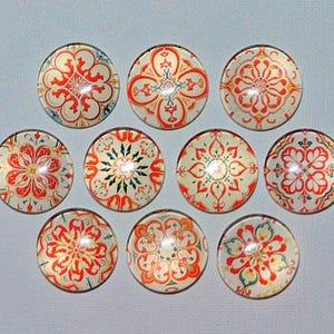 May include: A collection of ten round glass cabochons with intricate floral and geometric designs in red, orange, and blue on a cream background. The cabochons are arranged in a grid pattern.