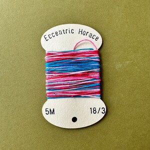 May include: A spool of pink, blue and white embroidery floss with the label "Eccentric Horace" and the measurements "5M" and "18/3".