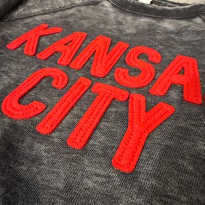 May include: A grey sweatshirt with a red embroidered "KANSAS CITY" graphic.