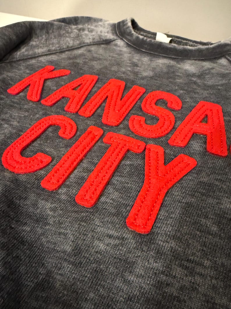 May include: A grey sweatshirt with a red embroidered "KANSAS CITY" graphic.