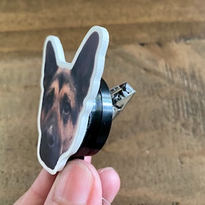 May include: A white plastic badge holder with a printed image of a German Shepherd dog's head. The holder is attached to a black retractable badge reel with a silver clip.
