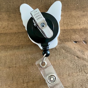 May include: White bulldog-shaped retractable badge holder with a black clip and a clear plastic badge holder.