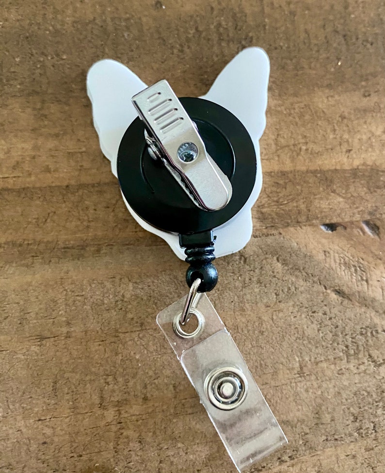 May include: White bulldog-shaped retractable badge holder with a black clip and a clear plastic badge holder.