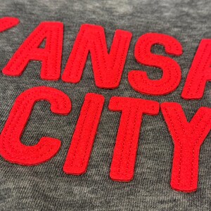 May include: A grey sweatshirt with the words "KANSAS CITY" in red embroidered lettering.