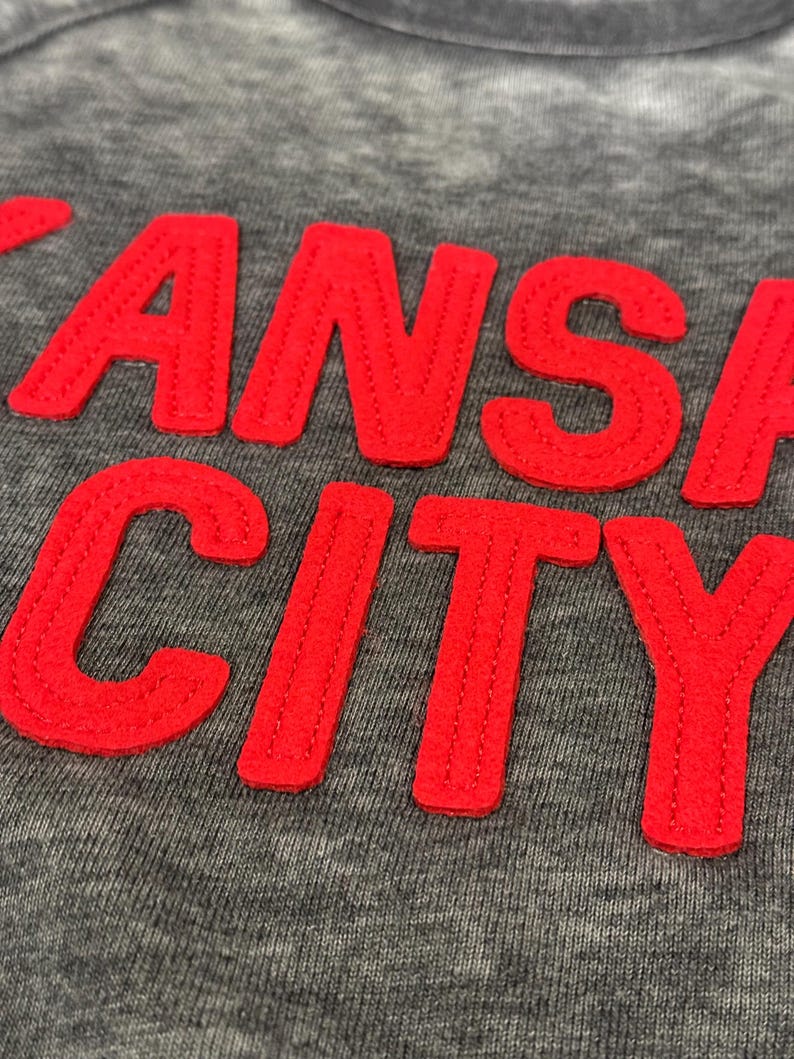 May include: A grey sweatshirt with the words "KANSAS CITY" in red embroidered lettering.