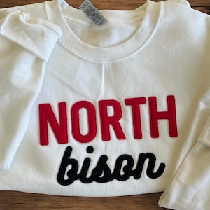 May include: White sweatshirt with red and black embroidered text that reads "NORTH bison".