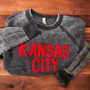 May include: A grey sweatshirt with a red embroidered design that says "KANSAS CITY".