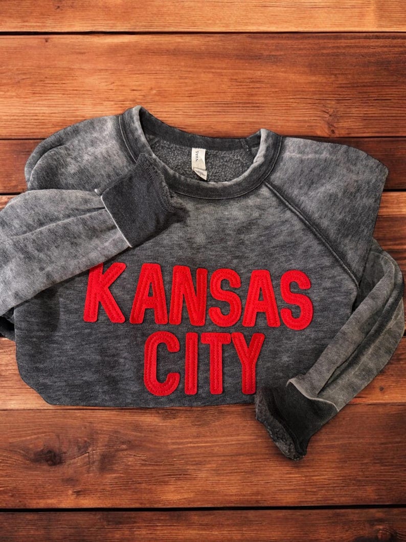 May include: A grey sweatshirt with a red embroidered design that says "KANSAS CITY".