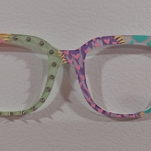 May include: A pair of colorful glasses with a pink, yellow, green, purple, and blue patterned design. The glasses have a unique, slightly jagged shape.