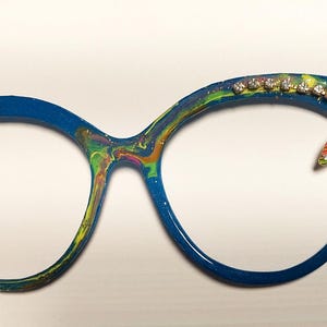 May include: Blue cat-eye glasses with a colorful swirl pattern and a gold dragonfly charm with rhinestones.