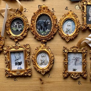 Puede incluir: Una colección de nueve retratos de animales en miniatura en marcos dorados ornamentados. La obra de arte incluye un ciervo, un mapache, un oso negro, un oso polar, un búho, una mofeta y un zorro. Cada marco tiene un diseño decorativo de estilo vintage.