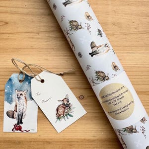 May include: A roll of woodland-themed gift wrap with illustrations of deer, birds, and foliage. Includes two gift tags with fox and deer illustrations. The gift wrap is 20" x 29" sheets. The text on the roll reads "Old Schoolhouse Art Woodland Holiday Gift Wrap".