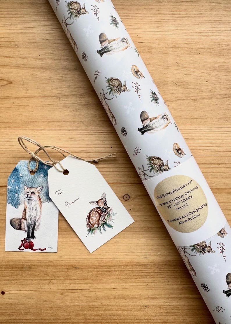 May include: A roll of woodland-themed gift wrap with illustrations of deer, birds, and foliage. Includes two gift tags with fox and deer illustrations. The gift wrap is 20" x 29" sheets. The text on the roll reads "Old Schoolhouse Art Woodland Holiday Gift Wrap".