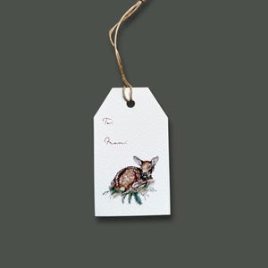 May include: White gift tag with a watercolor illustration of a fawn resting on pine needles. The tag has the words "To:" and "From:" in a handwritten font, and is attached to a natural twine string.