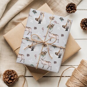 May include: Wrapped gift boxes with a light gray paper featuring foxes, deer, and winter foliage. The gifts are tied with twine and surrounded by pine cones and a roll of twine, creating a rustic, seasonal theme.