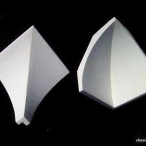 May include: Two white ceiling moulding pieces against a black backdrop. One is diamond-shaped with curved edges, the other triangular with a curved side. The website classicceiling.co.uk is visible in the bottom right corner.