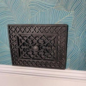 a decorative black metal piece with an intricate design, mounted on a wall with a blue and white patterned wallpaper.