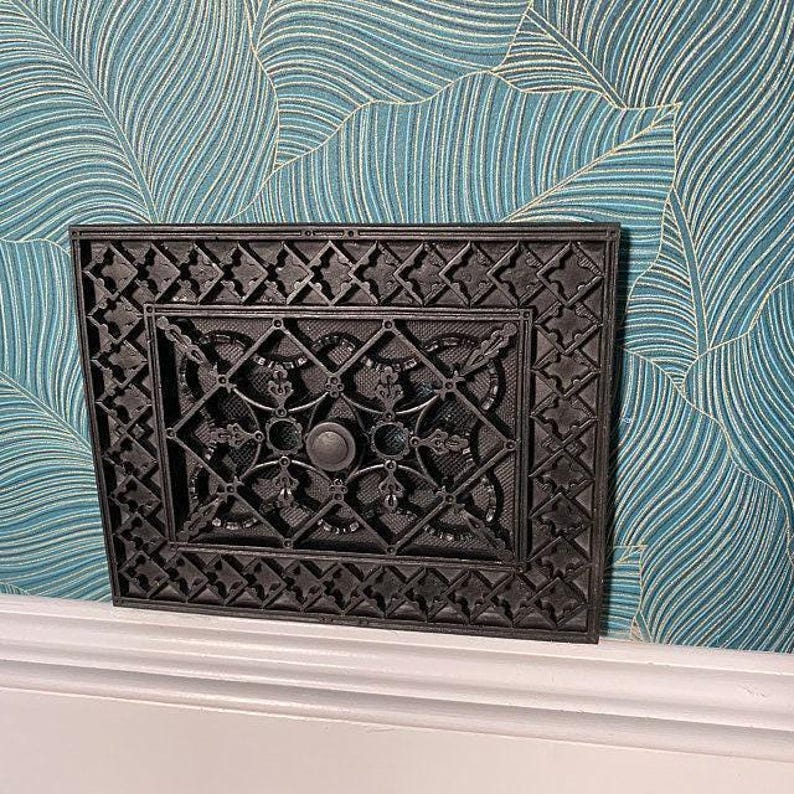 a decorative black metal piece with an intricate design, mounted on a wall with a blue and white patterned wallpaper.
