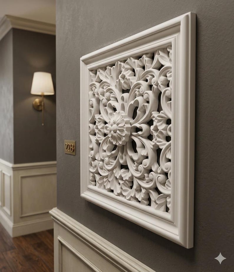 May include: A white, square wall decor piece with an ornate floral and leaf design. The decorative panel is framed and mounted on a gray wall. The intricate relief carving adds a touch of elegance to the interior.