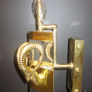 May include: A vintage wall sconce with a brass finish, featuring a ram's head design. The sconce has a clear glass section and a light bulb. The fixture is approximately 18 inches tall.