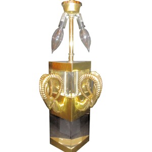 May include: A vintage brass table lamp with a geometric design. The lamp features a square base with gold accents and a black center section. Two decorative ram's horn shapes adorn the front. The lamp has three elongated light bulbs.