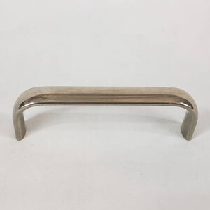 Op de afbeelding: Een zilveren metalen handvat met een gebogen vorm. Het handvat is ontworpen om een deur of lade te openen.