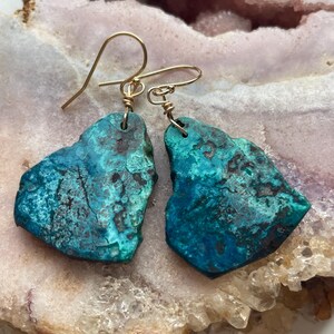 May include: A pair of turquoise blue earrings with gold wire wrapped around the edges. The earrings are shaped like irregular, freeform stones.
