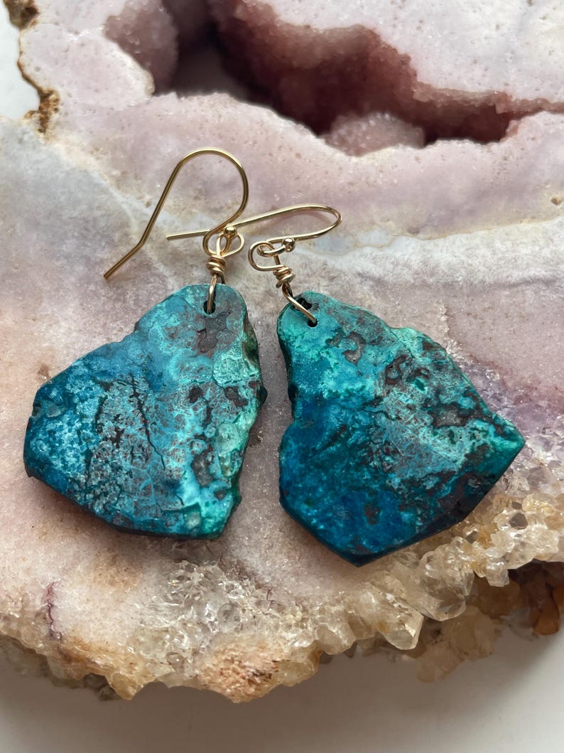 May include: A pair of turquoise blue earrings with gold wire wrapped around the edges. The earrings are shaped like irregular, freeform stones.