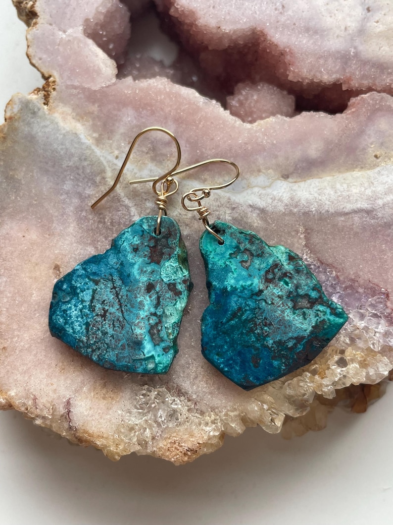 May include: A pair of turquoise green earrings with gold wire accents. The earrings are made of natural stone and have a unique, organic shape.