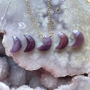 May include: A gold chain necklace with five purple crescent moon shaped gemstone pendants.