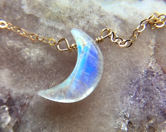 May include: A gold chain necklace with a crescent moon-shaped iridescent gemstone pendant.