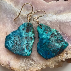 May include: A pair of turquoise blue earrings with gold wire accents. The earrings are made of natural stone and have a unique, organic shape.