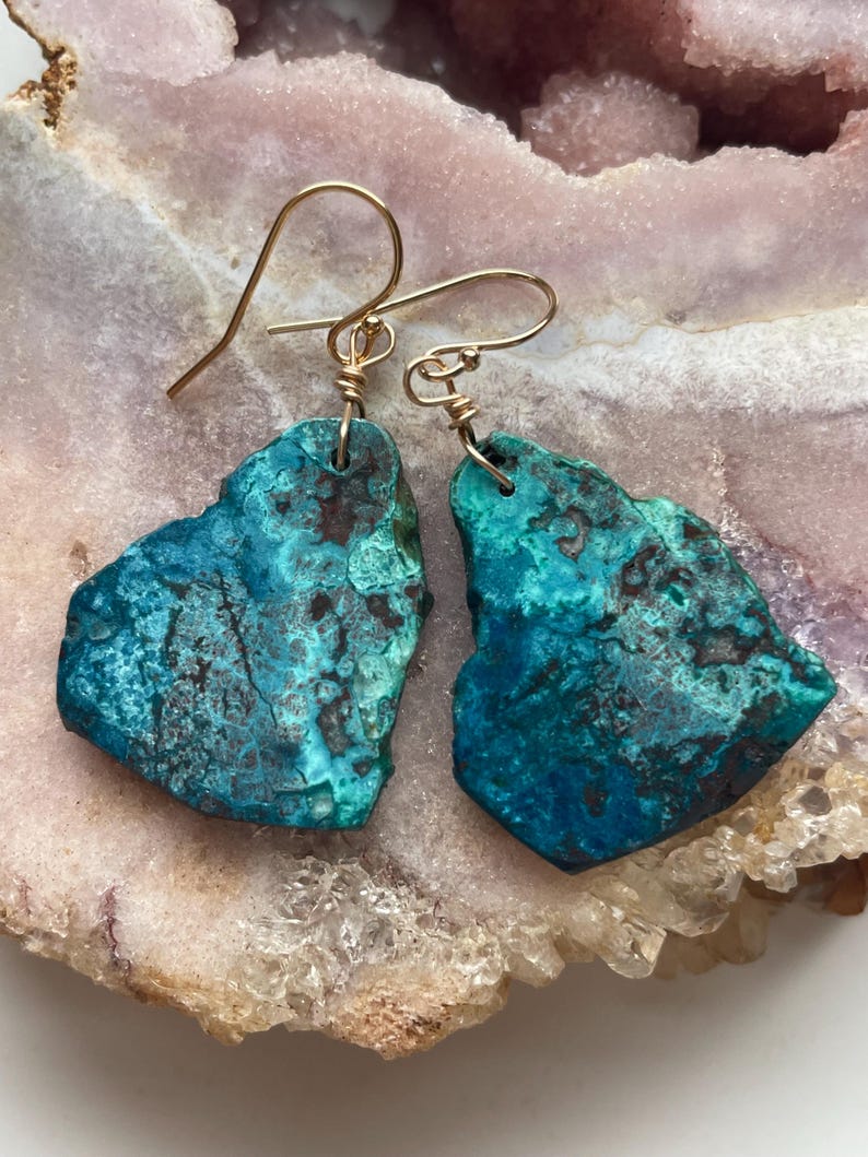 May include: A pair of turquoise blue earrings with gold wire accents. The earrings are made of natural stone and have a unique, organic shape.