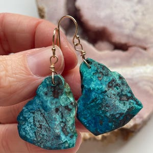 May include: A pair of turquoise green earrings with gold wire wrapped around the edges. The earrings are shaped like irregular, freeform pieces of stone.