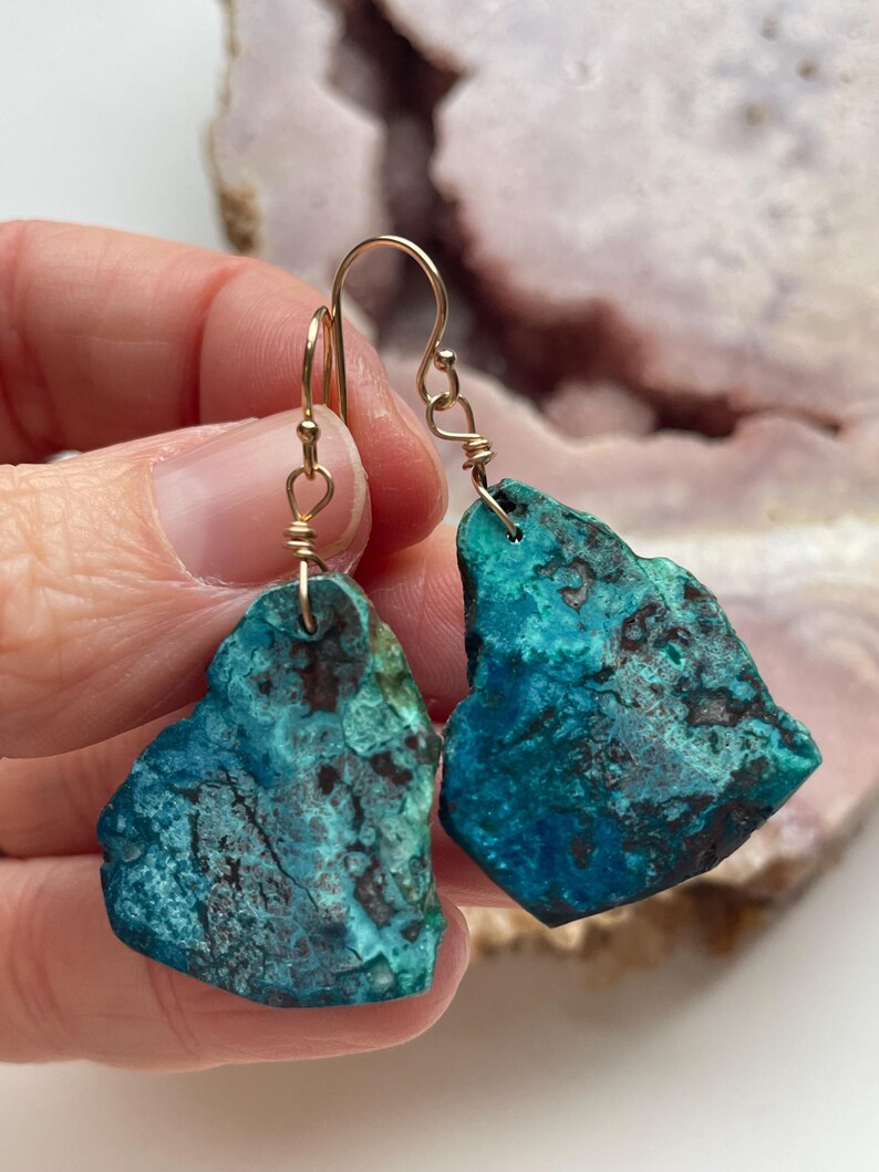May include: A pair of turquoise green earrings with gold wire wrapped around the edges. The earrings are shaped like irregular, freeform pieces of stone.